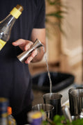 Bartender measuring a pour with a jigger — one of the 6 tools included in the leather bar roll