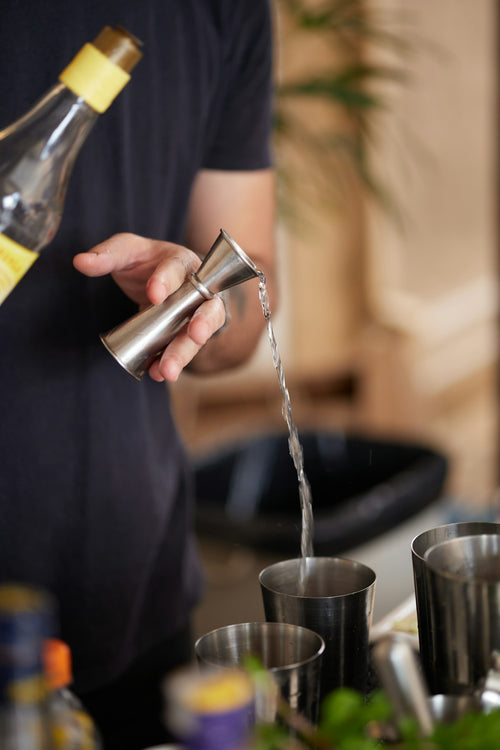 Bartender measuring a pour with a jigger — one of the 6 tools included in the leather bar roll